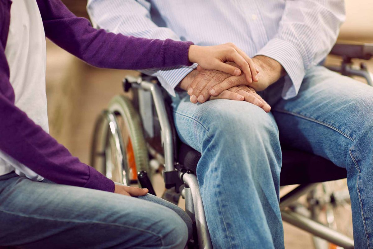 woman holding man's hand on his wheelchair