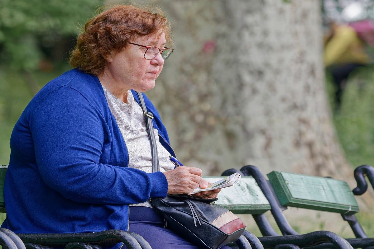 An elderly woman wears eye glasses and takes note, low vision